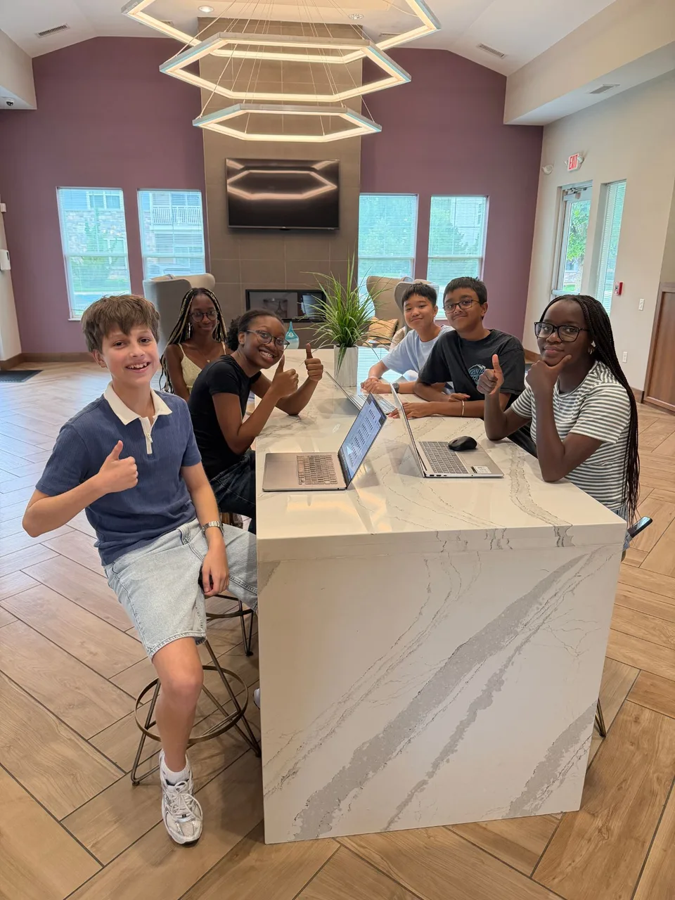 The Algebridge team around a counter with their laptops open, giving a thumbs up